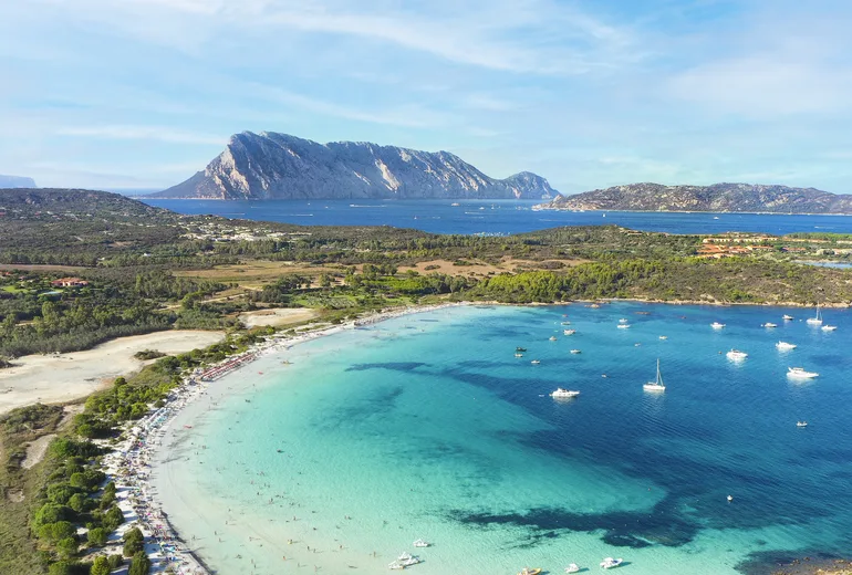 Aerial of a busy turquoise bay with anchored boats off Tavolara island, Sardinia, Italy