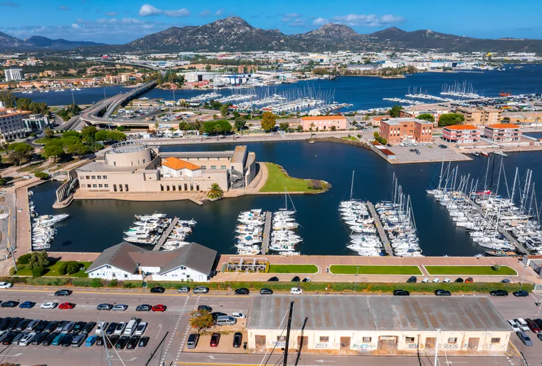 Aerial of Olbia waterfront, marina pontoons, city and mountains behind, Sardinia