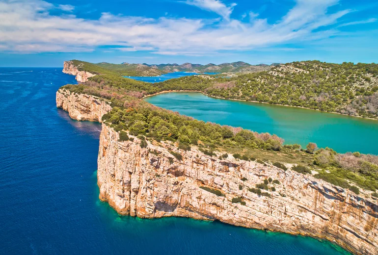 Aerial of Telascica cliffs dropping to sea beside green Mir lake, Dugi Otok