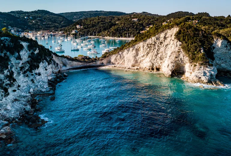 Aerial of white chalk cliffs with yacht-filled Lakka bay behind, Paxos