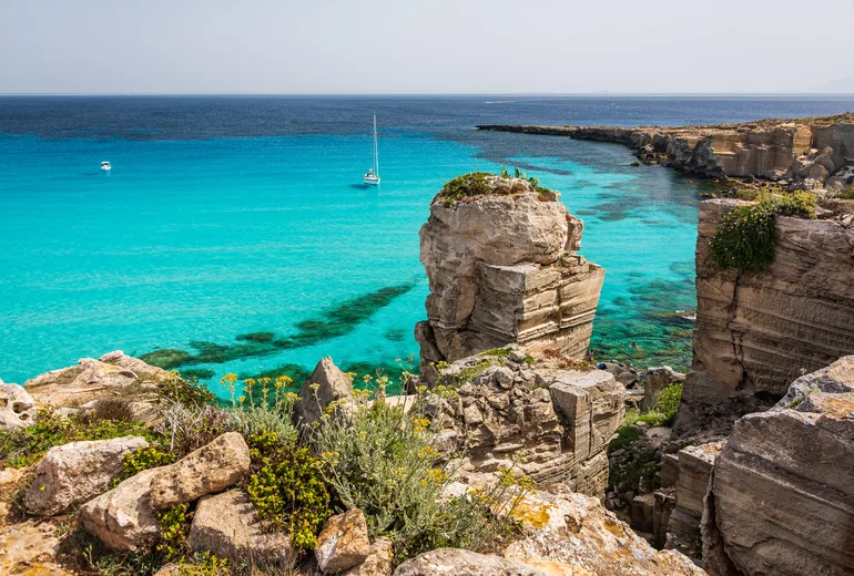 Anchored sailboat in turquoise Cala Rossa beneath limestone quarry cliffs, Favignana