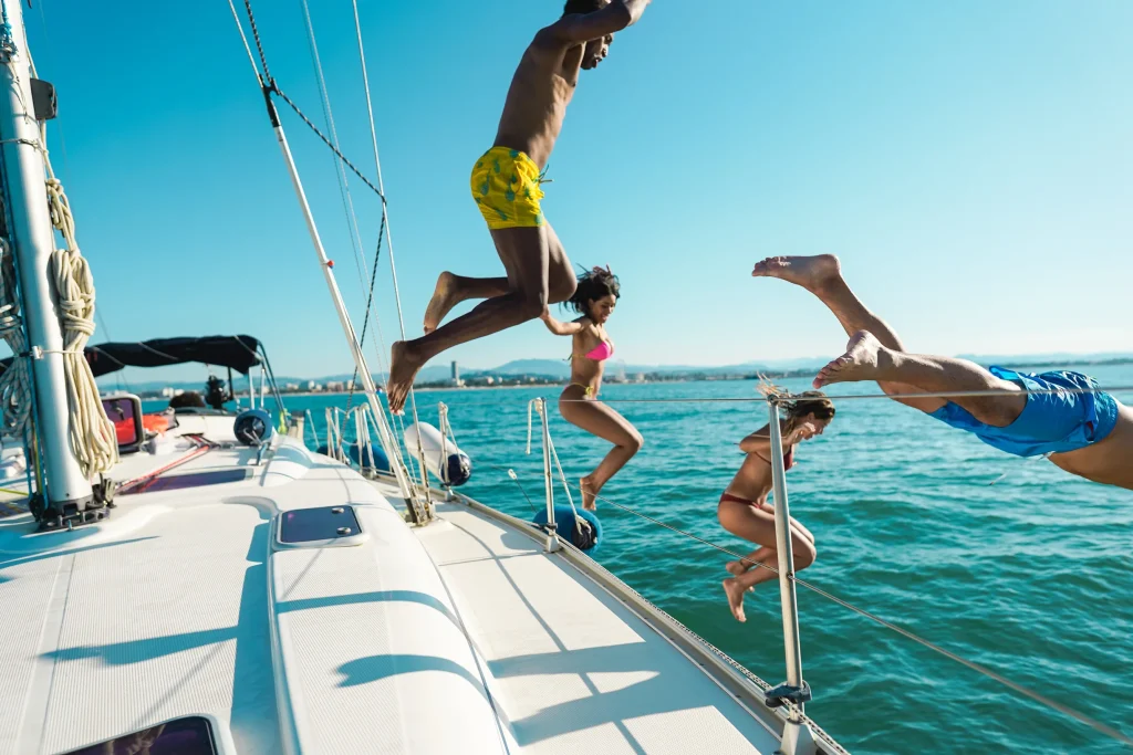 Group of friends diving off sailboat into sea on sunny day