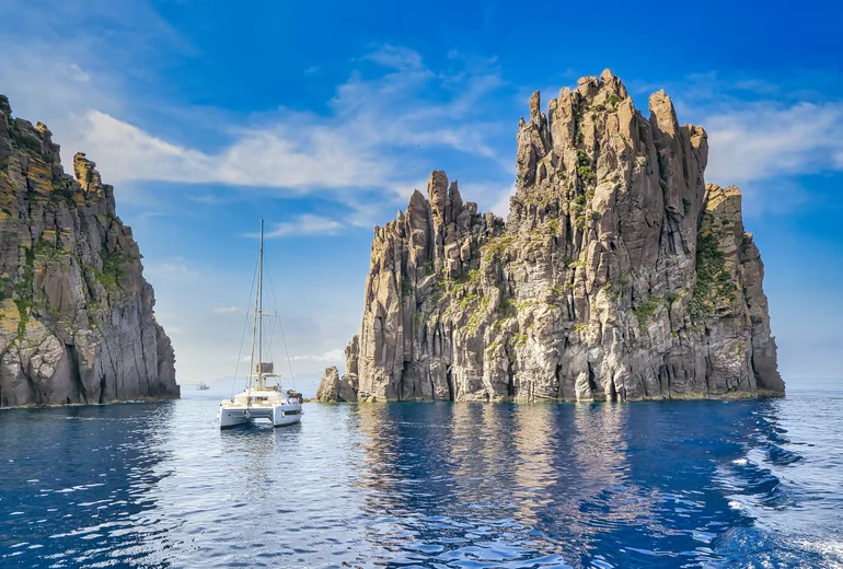 Catamaran anchored beside towering volcanic sea stacks, Aeolian Islands, Italy