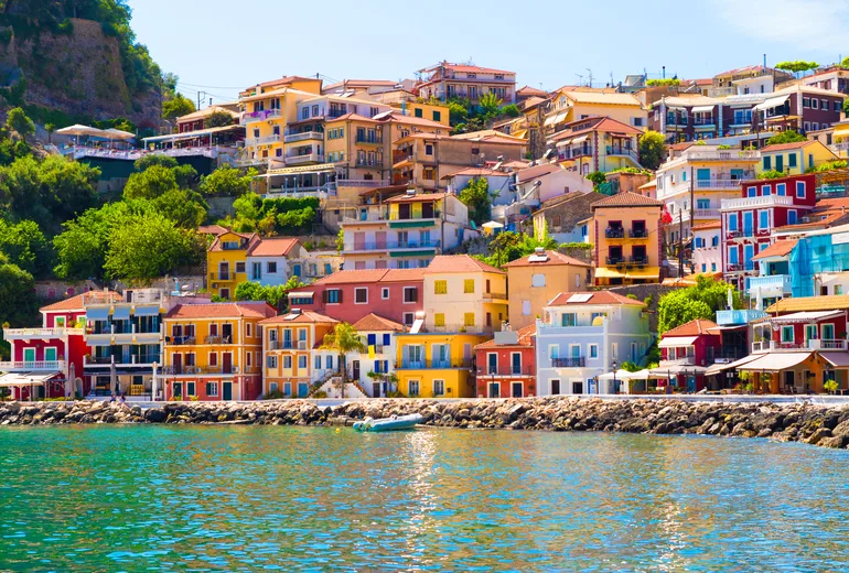 Colourful tiered houses of Parga rising above green harbour water, Greece