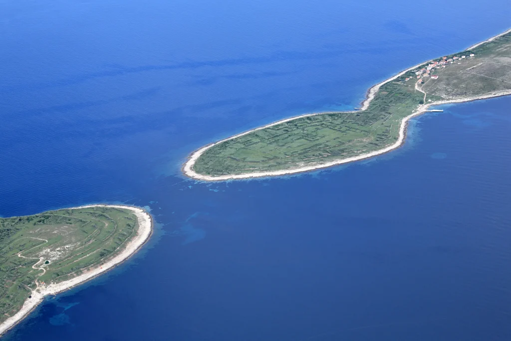 Aerial of flat green islets with stone field walls in blue sea