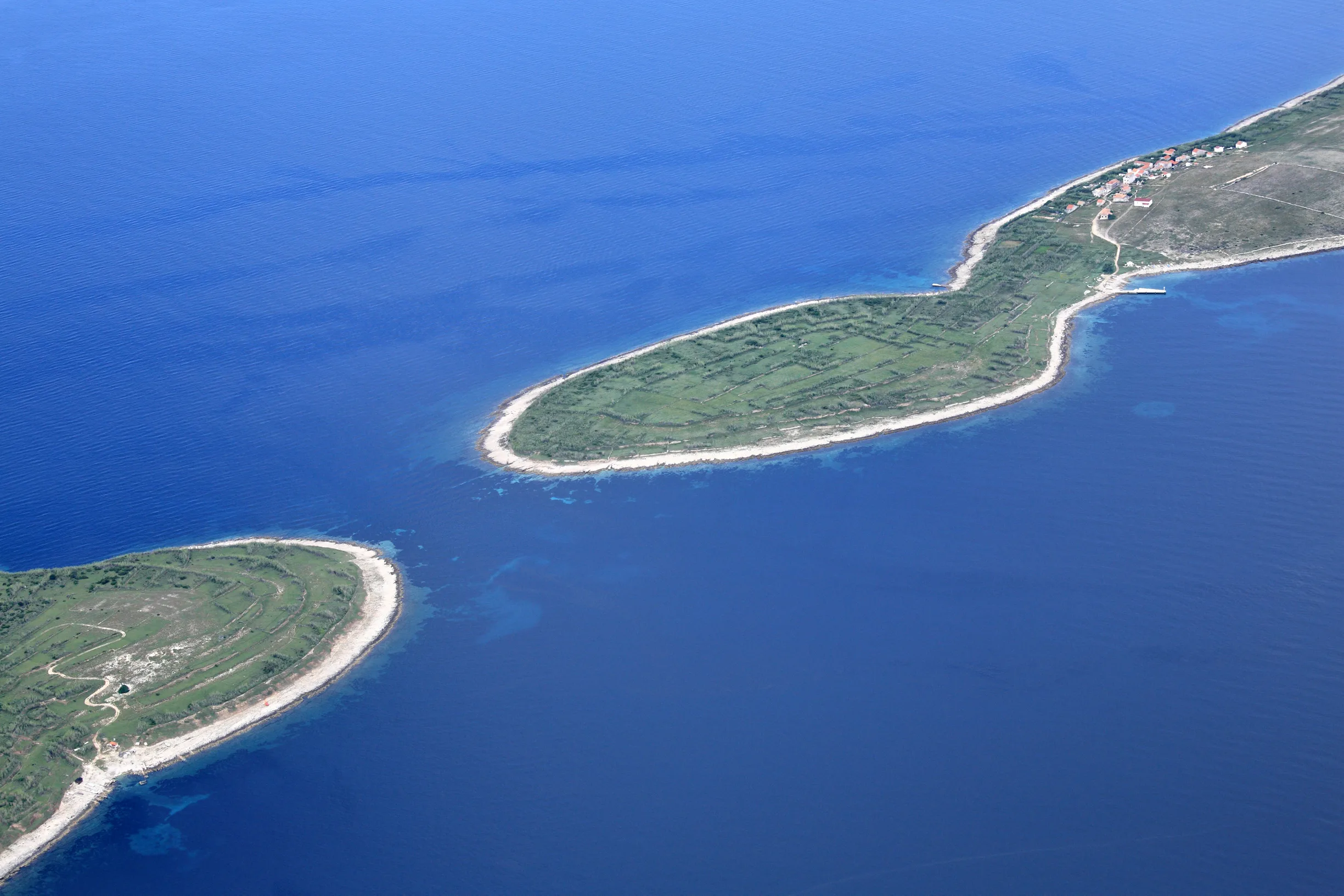 Aerial of flat green islets with stone field walls in blue sea