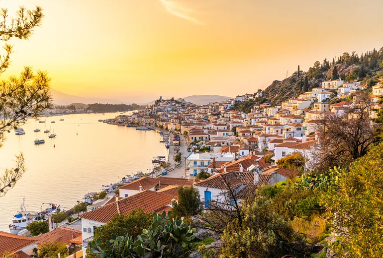Golden October sunset over Poros town rooftops and sailboats at anchor, Greece