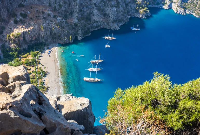 Gulets anchored in deep blue Butterfly Valley cove beneath sheer cliffs and beach