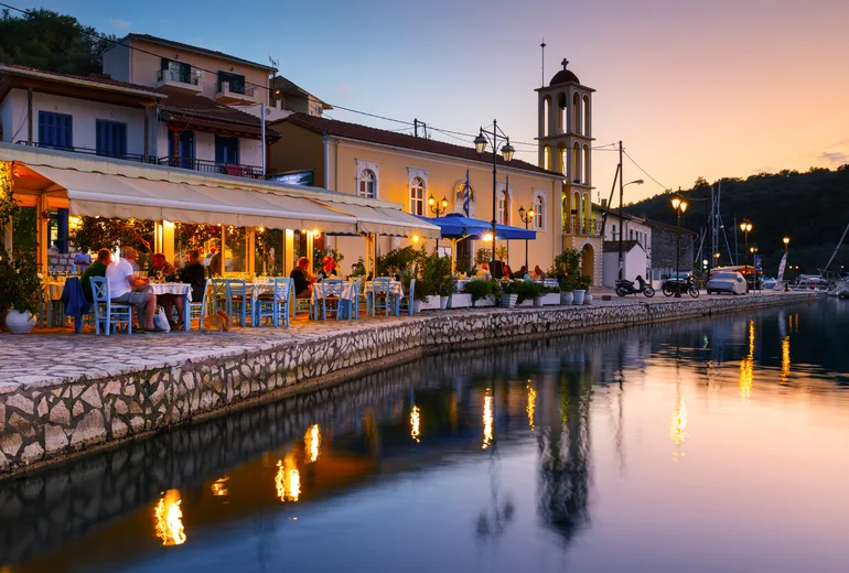 Harbourside tavernas and a church bell tower glowing at dusk in the Greek Ionian