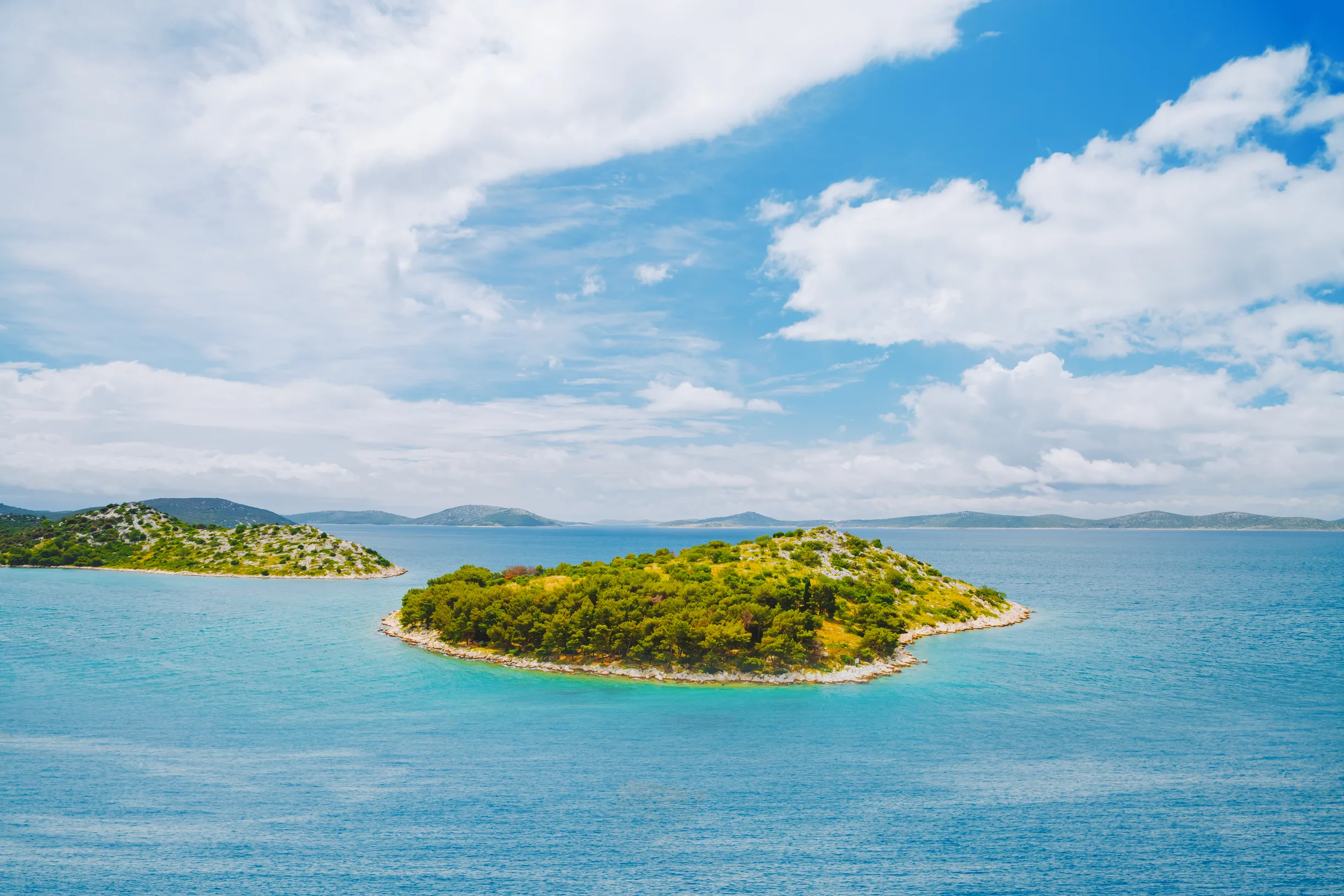 Small wooded islet with white pebble shore in calm island-dotted channel