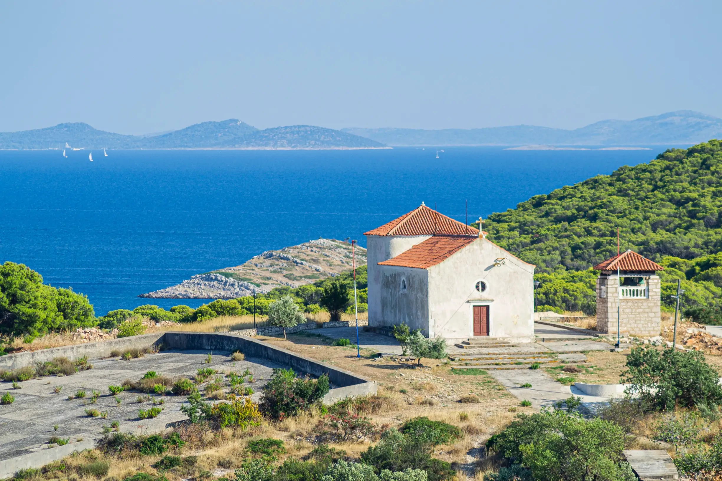 Stone church with red roof above blue sea and scattered islands