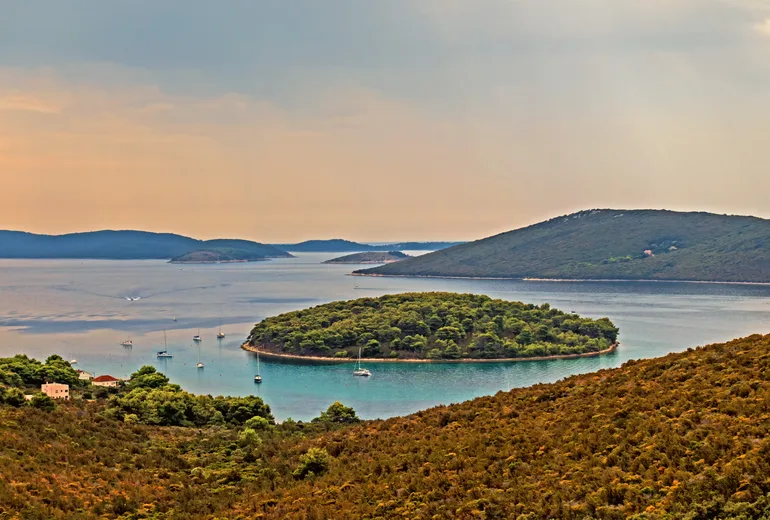 Sailboats anchored around a wooded islet at evening in Croatia