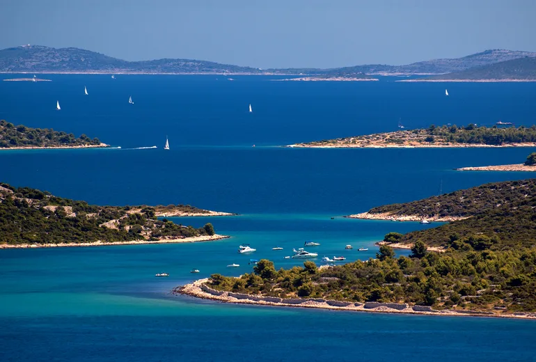 Sailboats with white sails scattered among the Adriatic islands on a deep blue sea