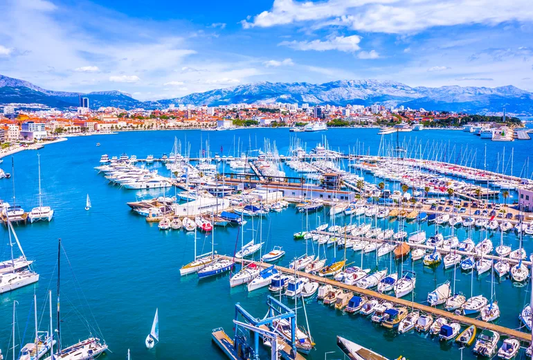 Split city marina packed with sailboats, mountains rising behind